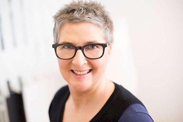 Woman with short hair and black glasses smiles at camera